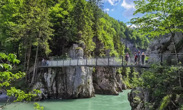Menschen überqueren eine Hängebrücke während einer entenlochklamm wanderung. Türkises Wasser fließt unter der Brücke hindurch, umgeben von steilen Felswänden und üppigem Grün.