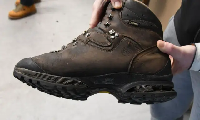 Brauner, abgenutzter Wanderschuh wird gehalten. Die Sohle ist stark abgenutzt, was zeigt, dass die Schuhe besohlen lassen werden müssen, um sie wieder einsatzfähig zu machen.