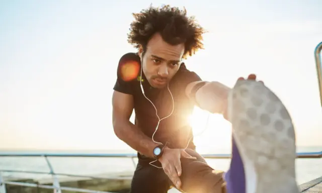 Mann dehnt sich am Meer, wichtig für die Regeneration nach Halbmarathon.
