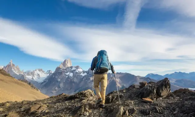 Ein Wanderer mit Rucksack und Stöcken erklimmt einen felsigen Grat. Die majestätische Bergkulisse zeigt die wahre trekking bedeutung: Abenteuer und Freiheit.