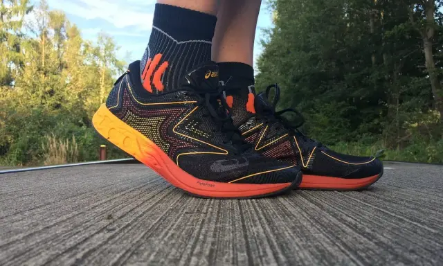 Asics Gel NoosaFast Laufschuhe in Schwarz mit orangen Akzenten, bereit für den nächsten Lauf im Grünen.