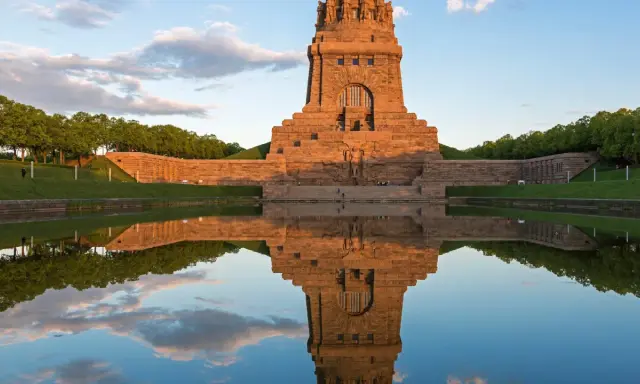 Das Völkerschlachtdenkmal in Leipzig spiegelt sich im Wasser. Ein Läufer genießt die Abendstimmung.
