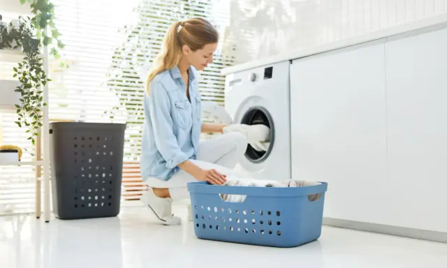 Frau lädt Wäsche in die Waschmaschine. So kann man eine Daunenjacke waschen ohne Trockner.