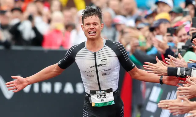 Triathlet Rico feiert seinen Zieleinlauf beim Ironman Luxembourg. Jubelnde Zuschauer reichen ihm die Hände.