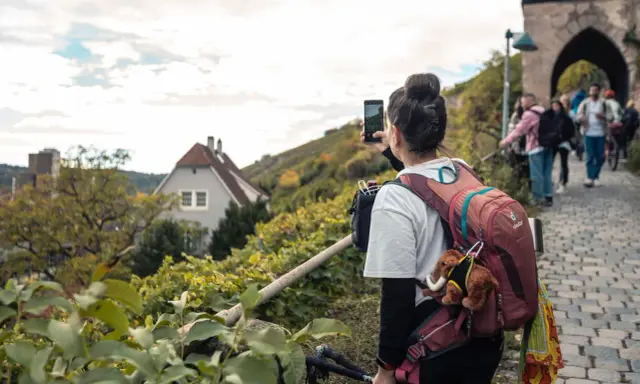 Frau macht Foto auf Wanderung bei Stuttgart. Weinberge und Häuser im Hintergrund.