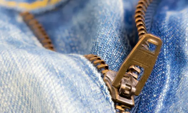 Nahaufnahme eines Reißverschlusses an Jeans. Der Schieber ist halb geöffnet. Ein guter Zeitpunkt, um den Reißverschluss reparieren zu lassen.