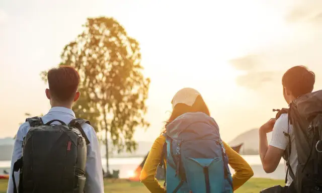 Drei Rucksackträger blicken auf den Bodensee. Die Sonne geht unter und taucht die Landschaft in warmes Licht. Eine perfekte Kulisse für eine Wanderung am Bodensee.