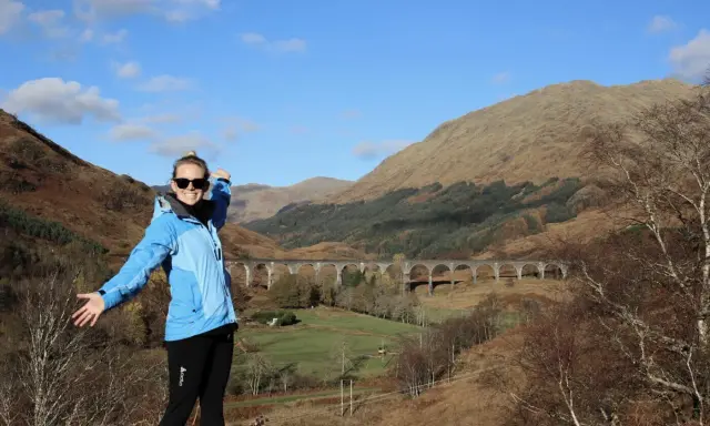 Glückliche Frau genießt das Wandern in Schottland vor einer beeindruckenden Brücke in den Highlands.