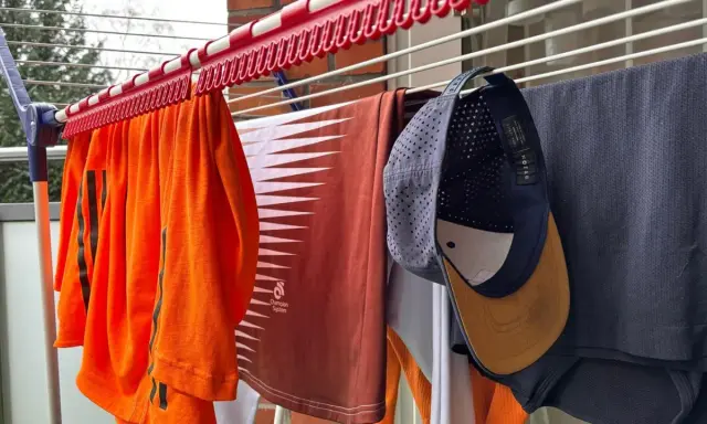 Wäscheleine mit Kleidung, darunter ein orangefarbenes Shirt, ein braunes Shirt und eine Kappe, die zum cap reinigen aufgehängt wurde.