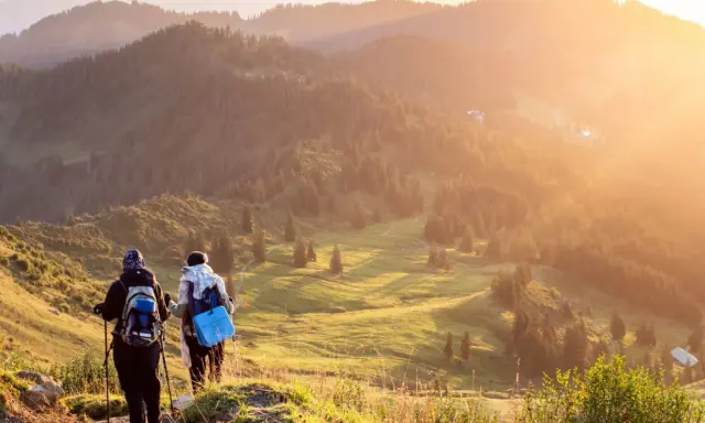 Zwei Wanderer genießen einen **great trail** in Kanada. Die Sonne taucht die bewaldeten Hügel in goldenes Licht.