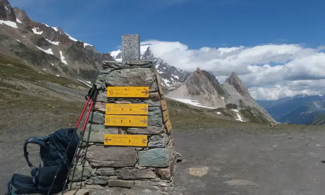 Wegweiser für die Tour du Mont Blanc Etappen: Rucksack und Stöcke liegen bereit. Bergpanorama mit blauen Himmel und Wolken.
