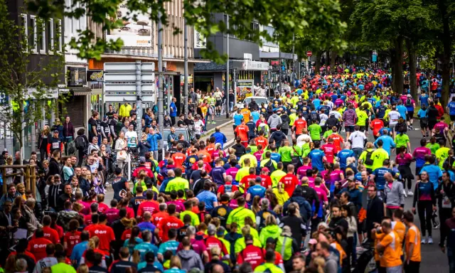 Große Menschenmenge beim Firmenlauf Essen, viele Läufer in bunten Trikots auf einer Straße, umgeben von Bäumen und Gebäuden.