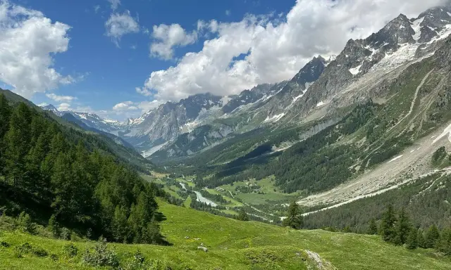 Grüne Almwiesen und Nadelwälder säumen das Tal auf einer Montblanc Tour. Majestätische Berge mit Schneefeldern ragen in den blauen Himmel.