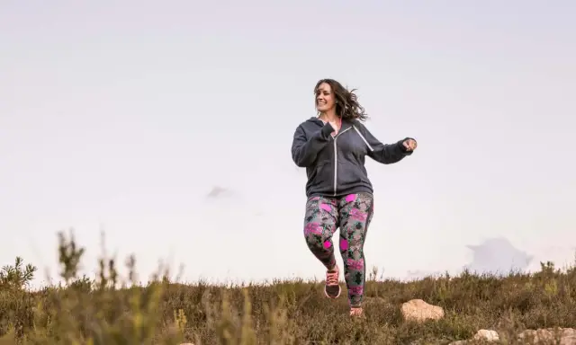 Frau joggt mit Gewichten in bunter Hose durch die Natur.