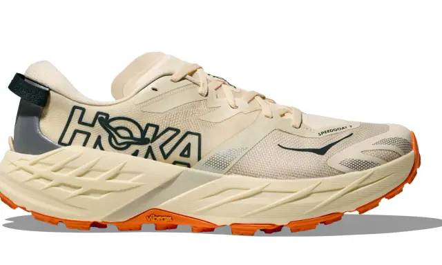 Beiger Hoka Speedgoat 7 Trailrunningschuh mit orangefarbener Vibram-Sohle und dunklem Hoka-Logo.