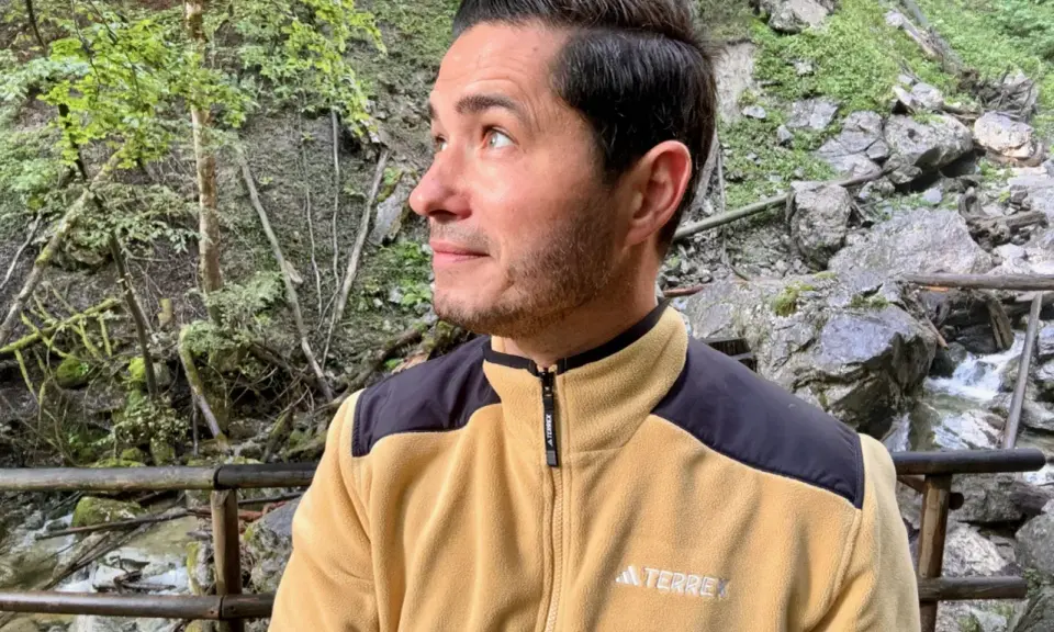 Mann in gelber Fleecejacke mit schwarzem Kragen und Schulterpartien, die zeigt, welche Fleecejacke wirklich warm ist.