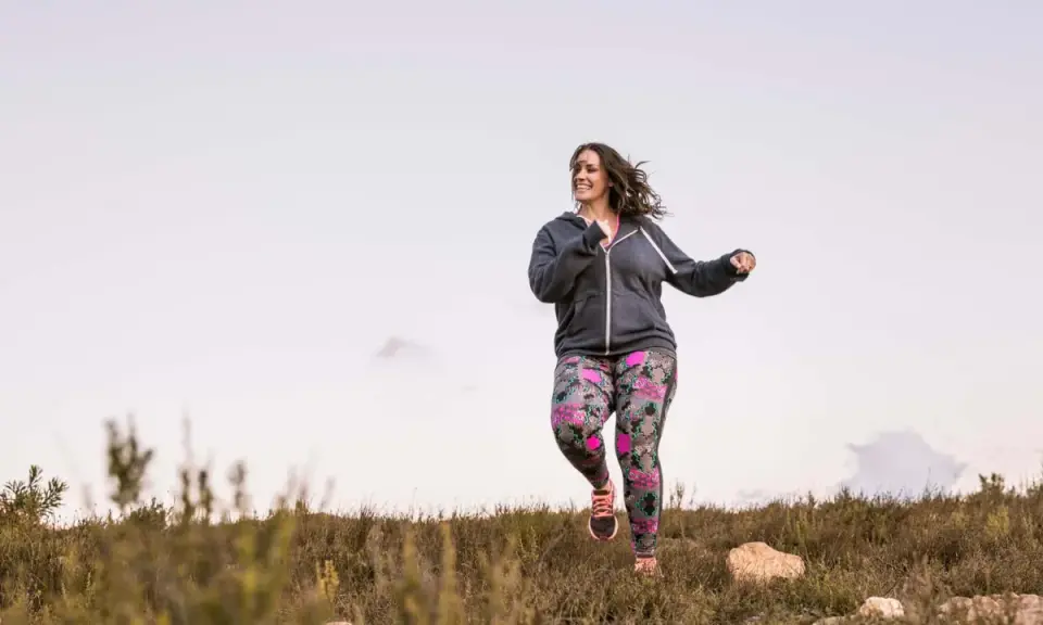 Frau joggt mit Gewichten in bunter Hose durch die Natur.