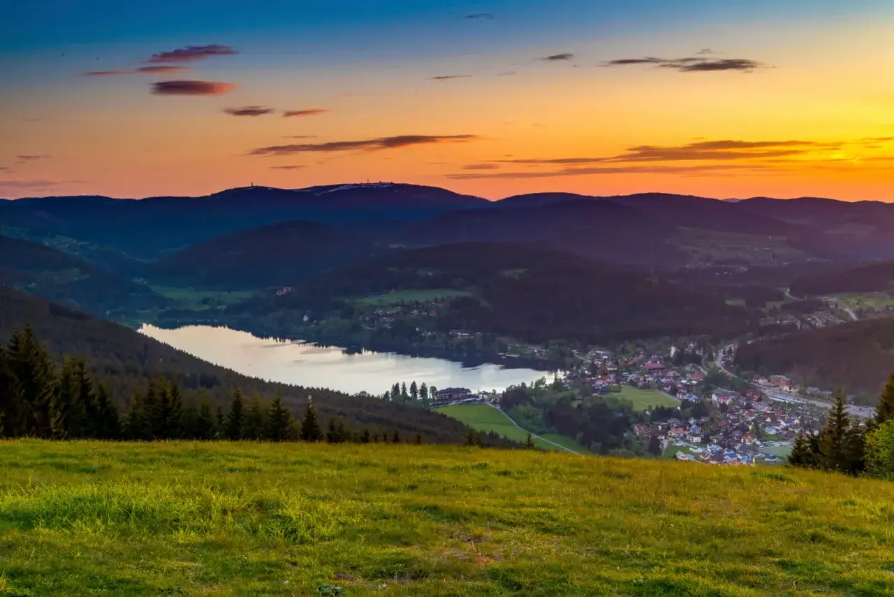 Sonnenuntergang &uuml;ber dem Titisee im Schwarzwald. Perfekt f&uuml;r Wandertouren, mit malerischen H&uuml;geln und einem Dorf am Seeufer.