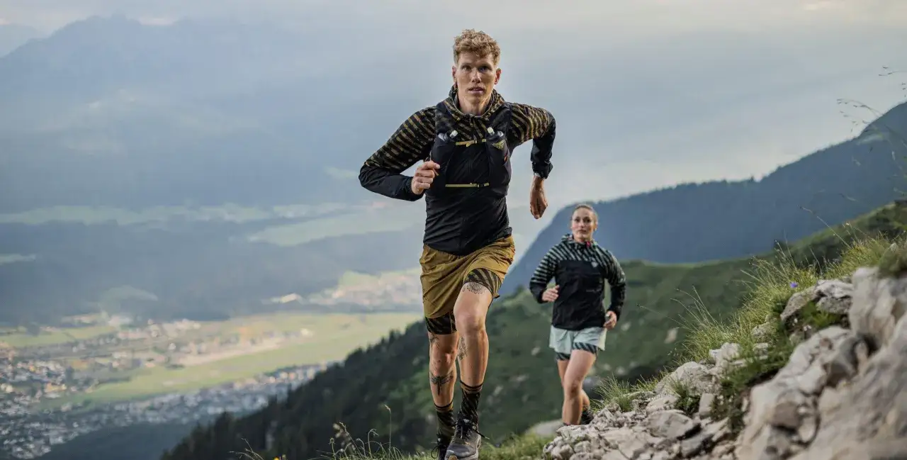 Zwei Läufer auf einem Bergpfad, bereit für einen Ultramarathon in Deutschland. Die Landschaft ist atemberaubend.