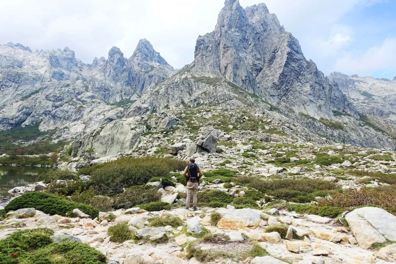 Wanderer auf dem korsika weitwanderweg blickt auf eine dramatische Berglandschaft mit einem Bergsee.