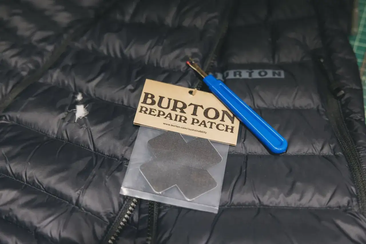 Schwarze Polyester Jacke mit Rissen, bereit für ein Burton Reparatur-Patch. Ein Nahttrenner liegt bereit.