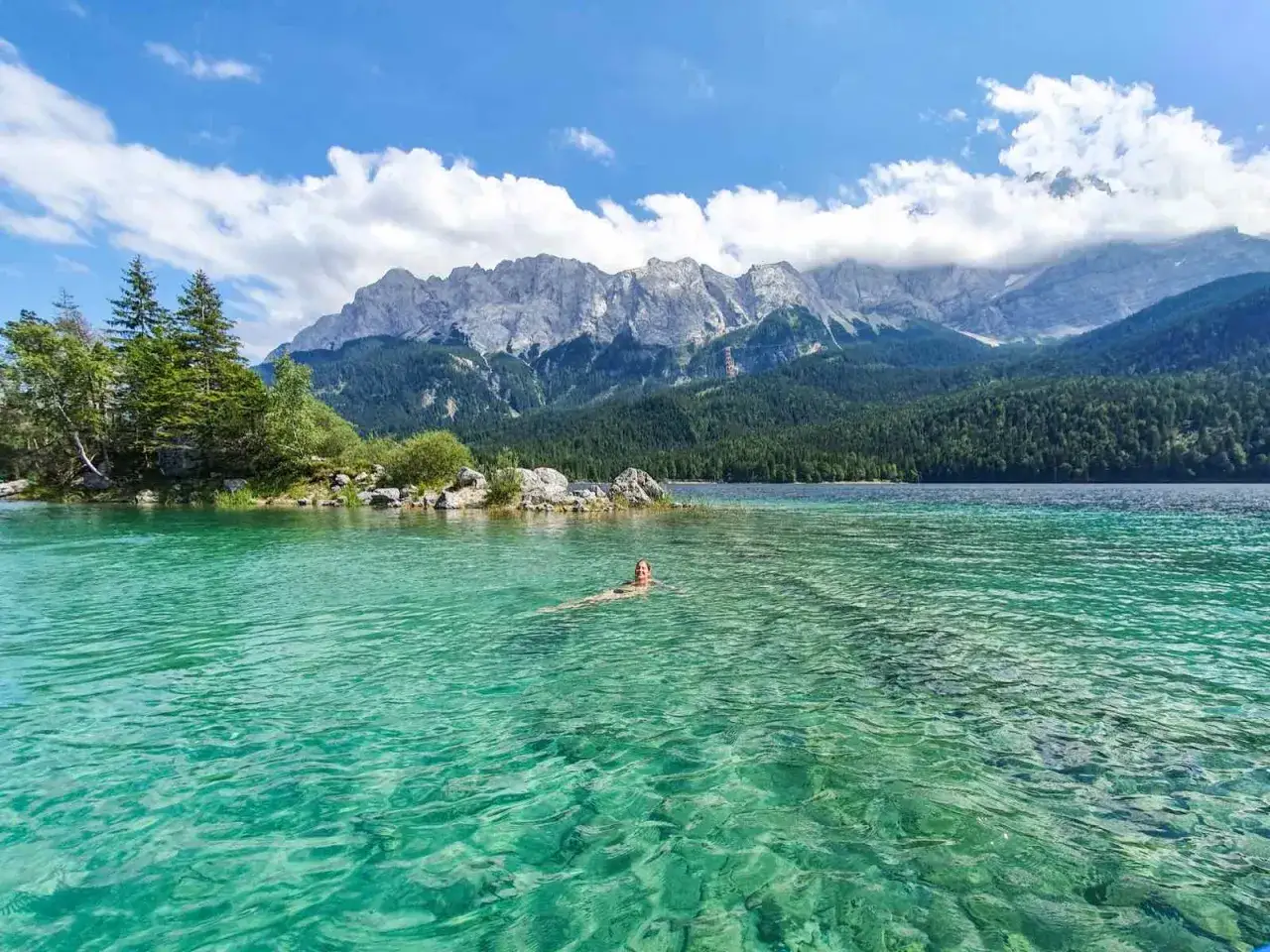 Eine Person schwimmt im kristallklaren Wasser des Eibsees, umgeben von grünen Wäldern und majestätischen Bergen. Der Eibsee Rundweg lädt zu solchen Erlebnissen ein.