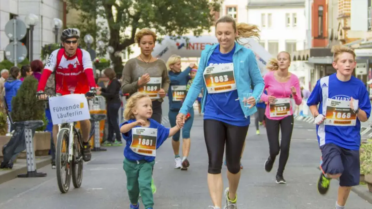 Familien beim Sommernachtslauf Limburg. Ein Radfahrer führt, während eine Mutter mit ihrem Kind und andere Läufer die Strecke entlang rennen.