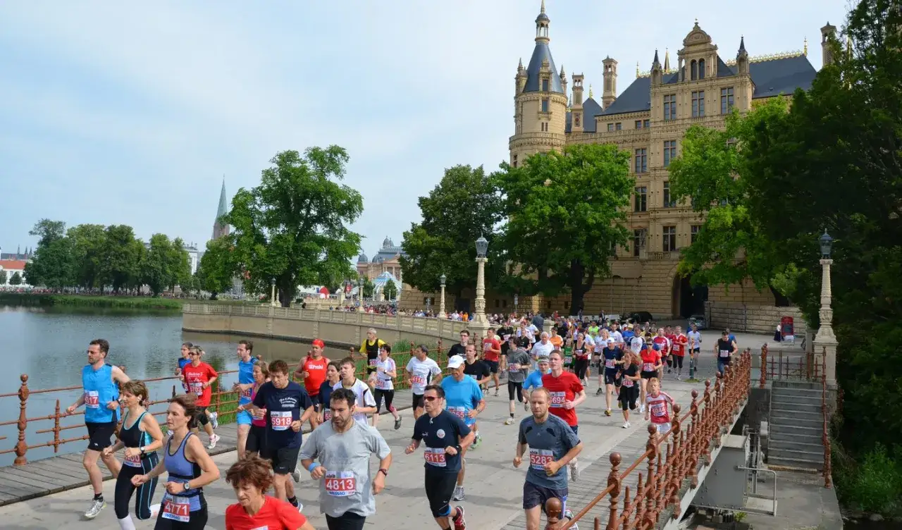 Läufer beim 5-Seen-Lauf in Schwerin überqueren eine Brücke vor dem Schloss.