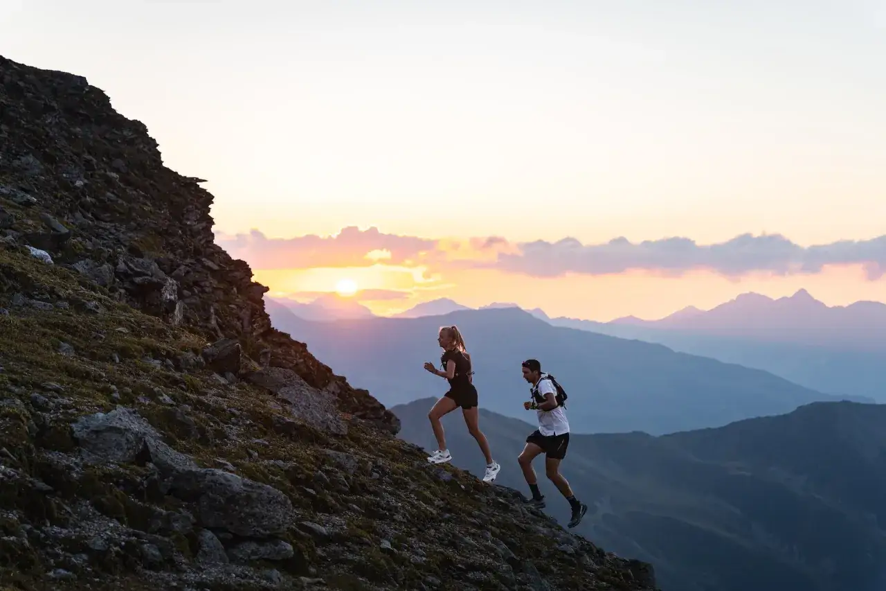 Zwei Läufer erklimmen einen felsigen Hang im Abendlicht. Perfekte trailrunning termine für ein unvergessliches Erlebnis.