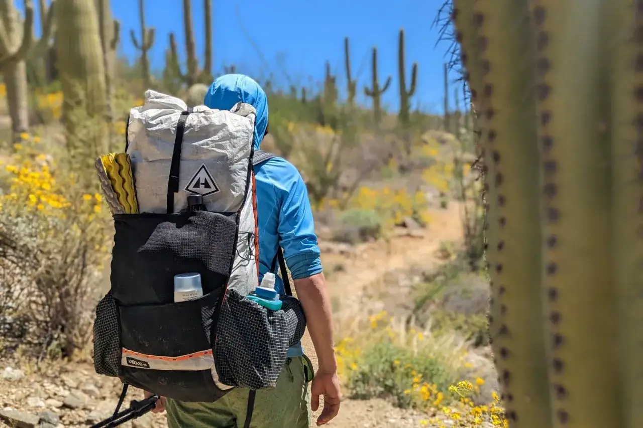 Person mit ultralight trekking Rucksack wandert durch eine Wüste mit Kakteen und gelben Blumen.