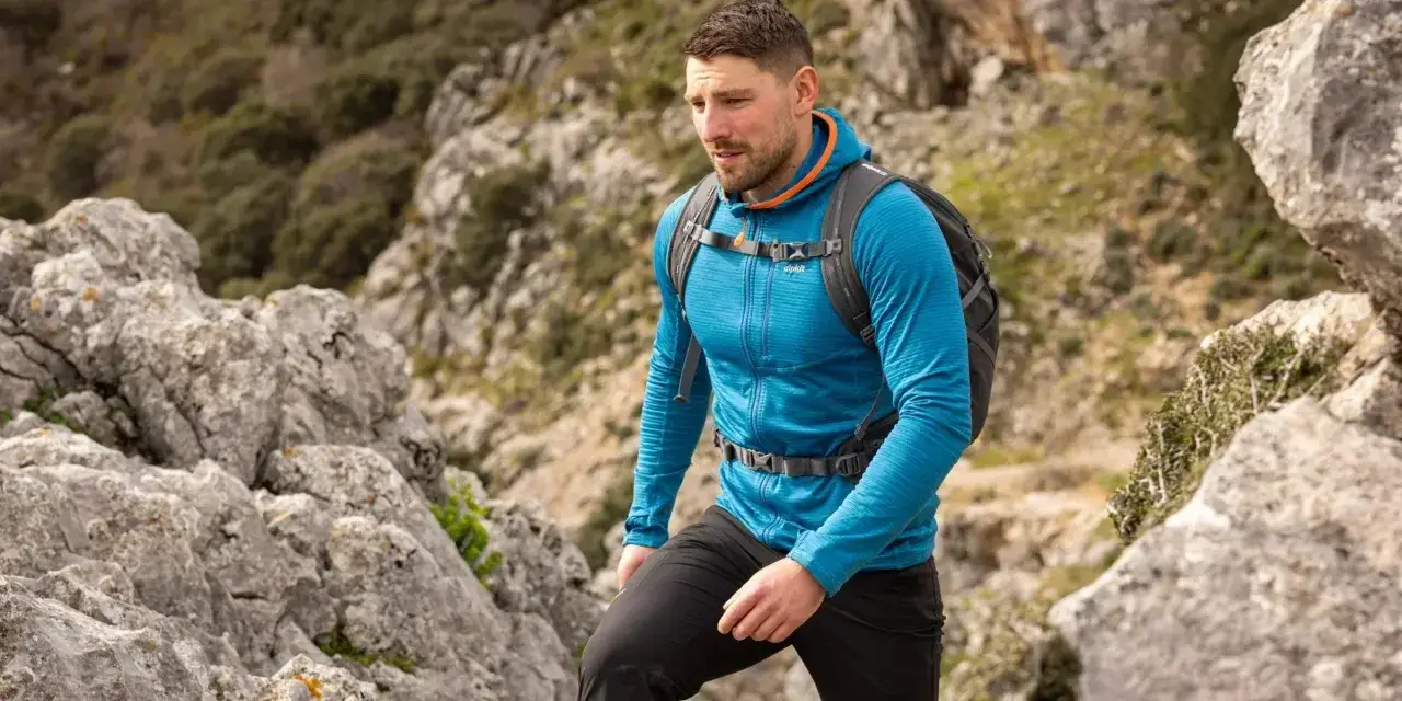 Ein Mann wandert in einem blauen Midlayer mit Rei&szlig;verschluss und Kapuze durch felsiges Gel&auml;nde.