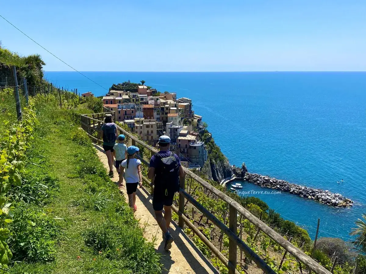 Familie wandert auf einem Küstenpfad mit Blick auf die bunten Häuser von Manarola. Hier liegt Cinque Terre, ein malerisches Dorf an der italienischen Riviera.