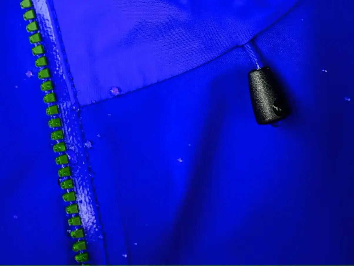 Blaue Goretex Jacke mit Reißverschluss und Wassertropfen. Die Jacke wird gewaschen, um ihre wasserabweisenden Eigenschaften zu erhalten.