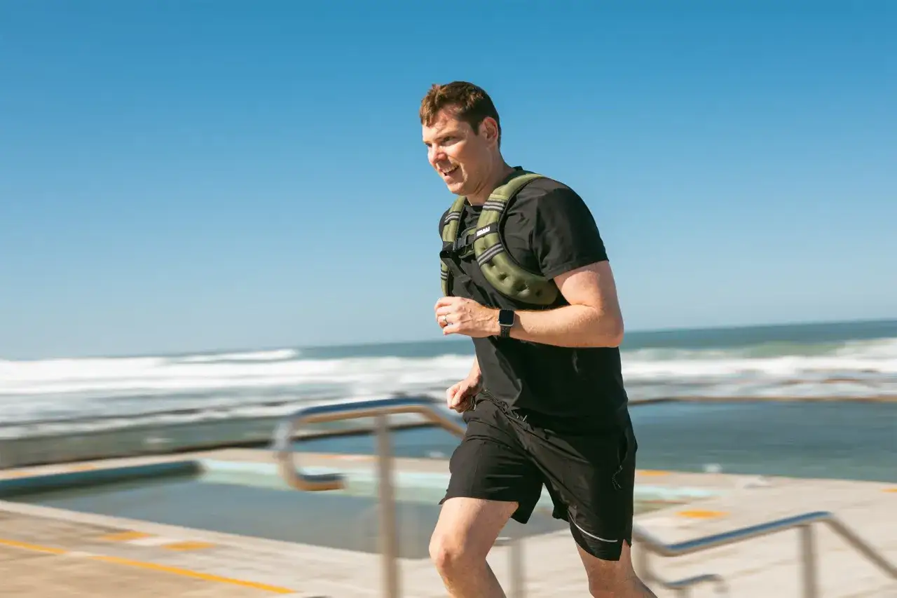 Mann joggt mit Gewichten am Meer entlang.