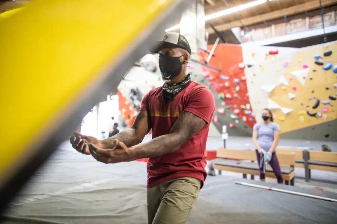 Mann in rotem Shirt, Khaki-Hose und Maske, bereit zum Bouldern. So was zieht man zum Bouldern an: bequeme Kleidung f&uuml;r Bewegung.