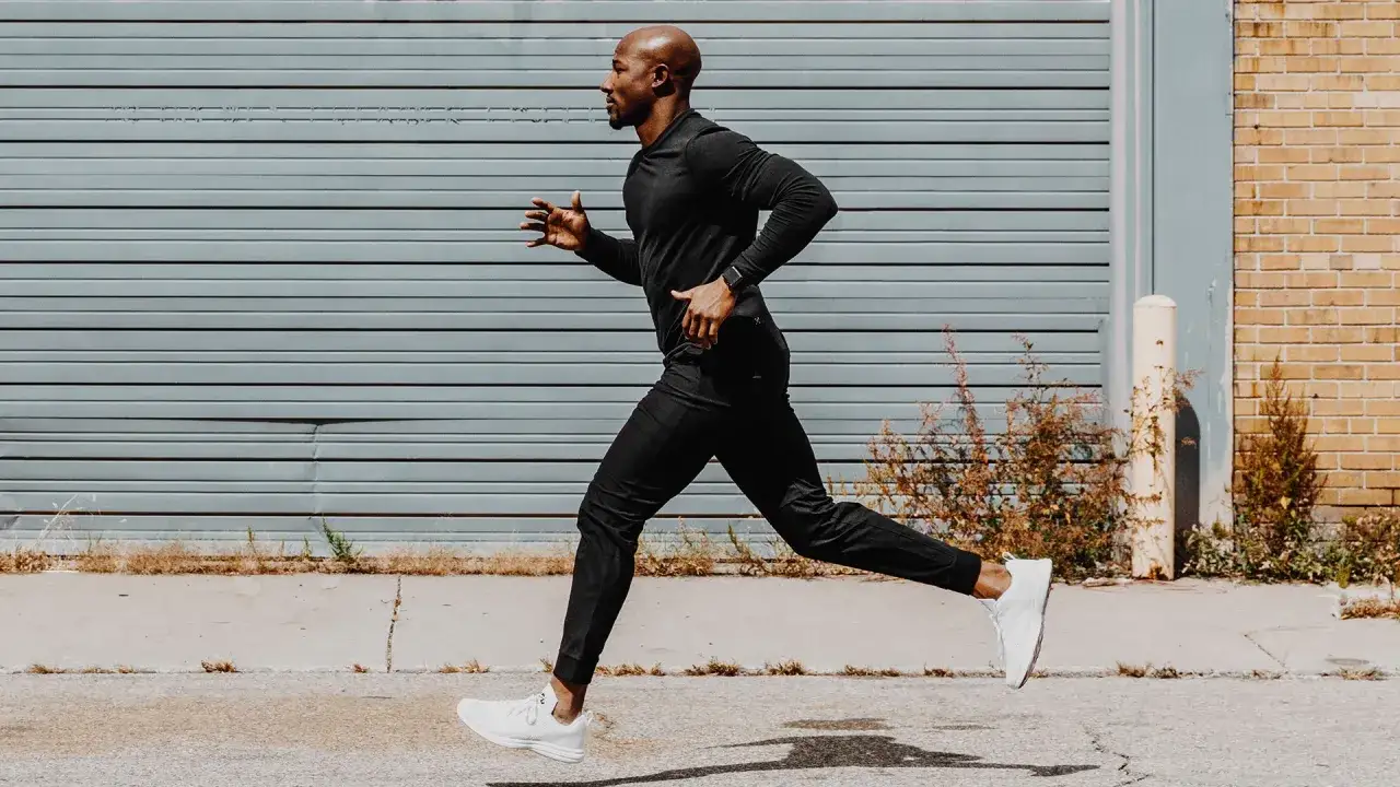 Ein Mann in schwarzer Sportkleidung macht slow jogging vor einer grauen Garagent&uuml;r.