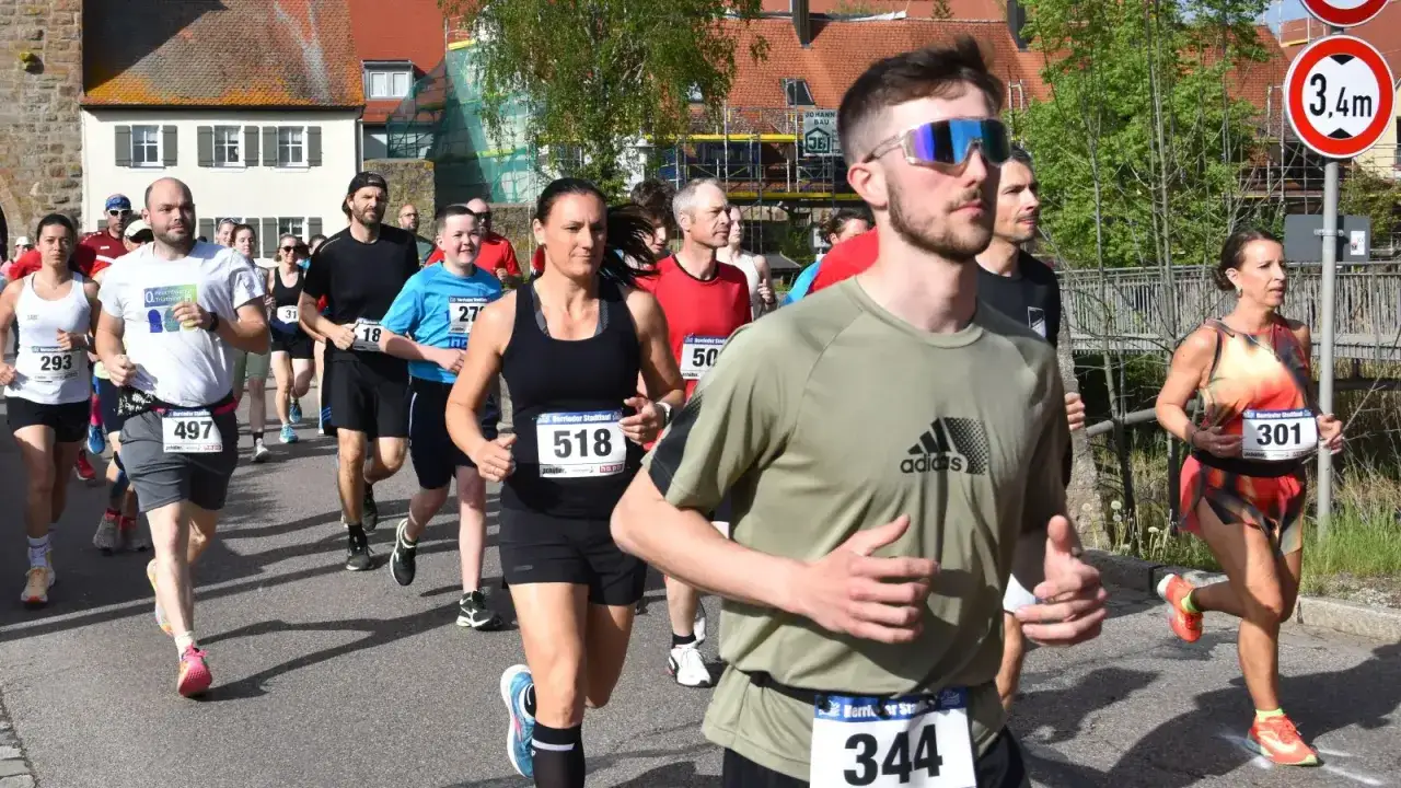 L&auml;ufer beim main city run. Ein Mann mit Sonnenbrille f&uuml;hrt die Gruppe an, gefolgt von vielen anderen Teilnehmern in Sportkleidung.