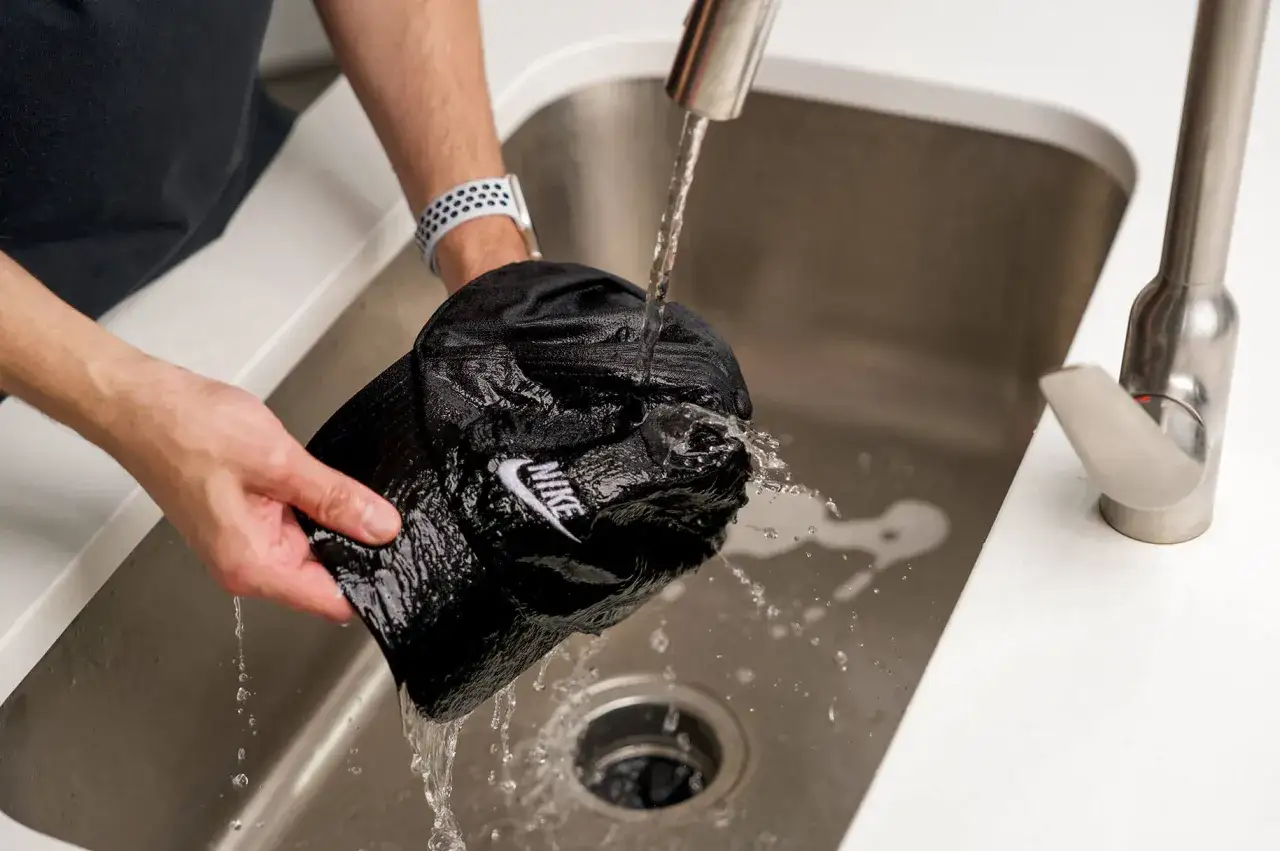 H&auml;nde reinigen eine schwarze Nike-Cap unter flie&szlig;endem Wasser im Sp&uuml;lbecken.