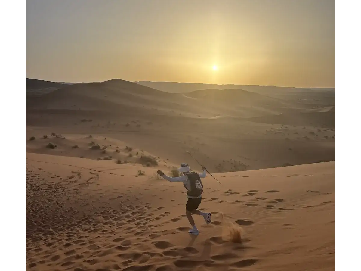 Läufer kämpft sich durch die Dünen des Marathon des Sables. Die Sonne geht unter und wirft lange Schatten.