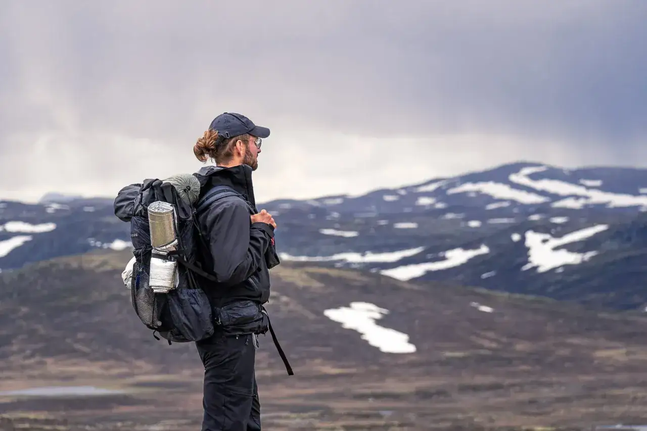 Ein Mann mit Rucksack blickt in die verschneite Berglandschaft. Das ist echtes Trekking, mehr als nur ein einfacher Wandertag.
