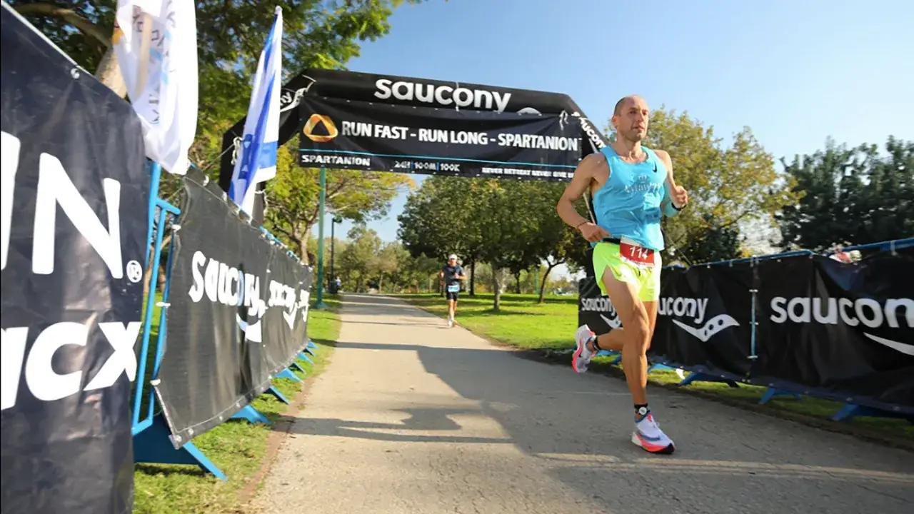 L&auml;ufer mit Startnummer 114 auf dem Weg zum ultramarathon weltrekord. Saucony-Banner s&auml;umen die Strecke.