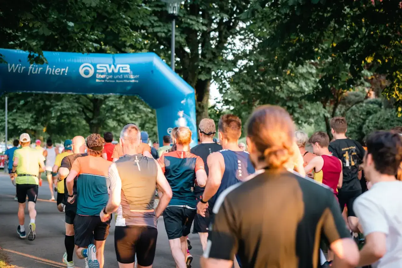 L&auml;ufer starten beim Bonner Nachtlauf unter einem blauen Torbogen.