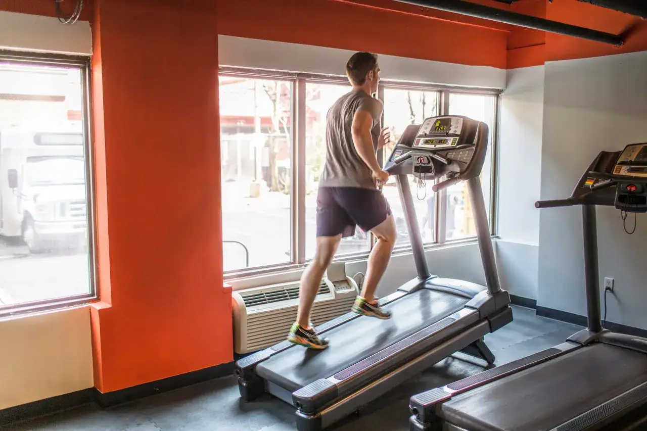 Mann im T-Shirt und Shorts trainiert auf einem Laufband. Das Laufbandtraining ist eine gute Cardio-Übung.