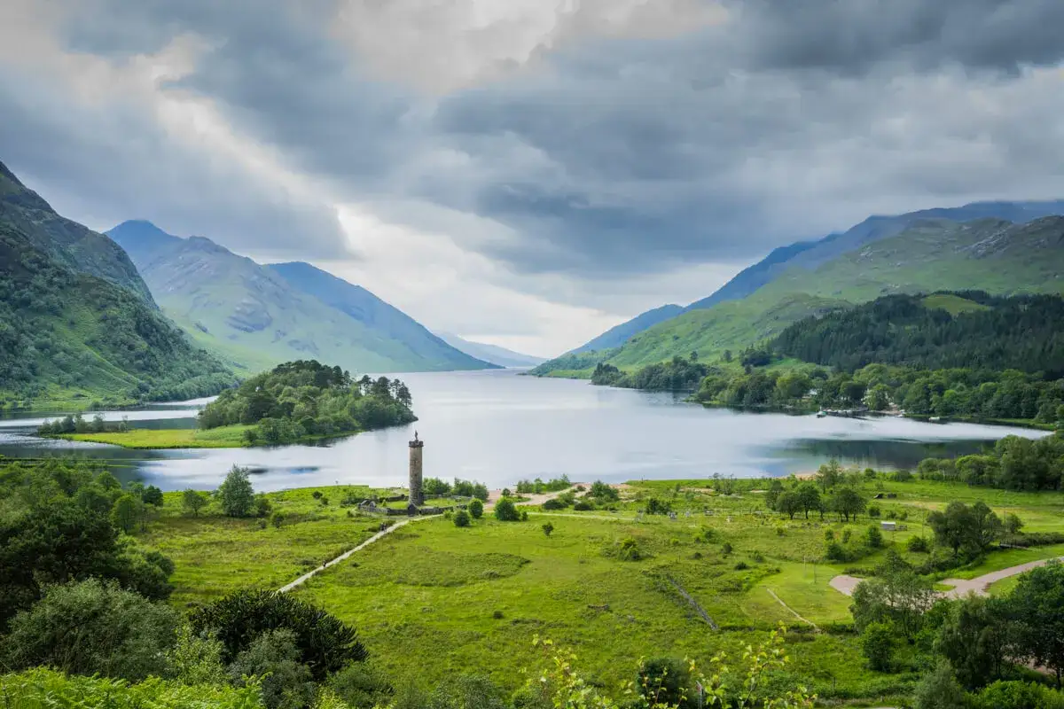 Ein malerischer See mit grünen Hügeln und einem Denkmal, perfekt für eine Wanderung in Schottland.
