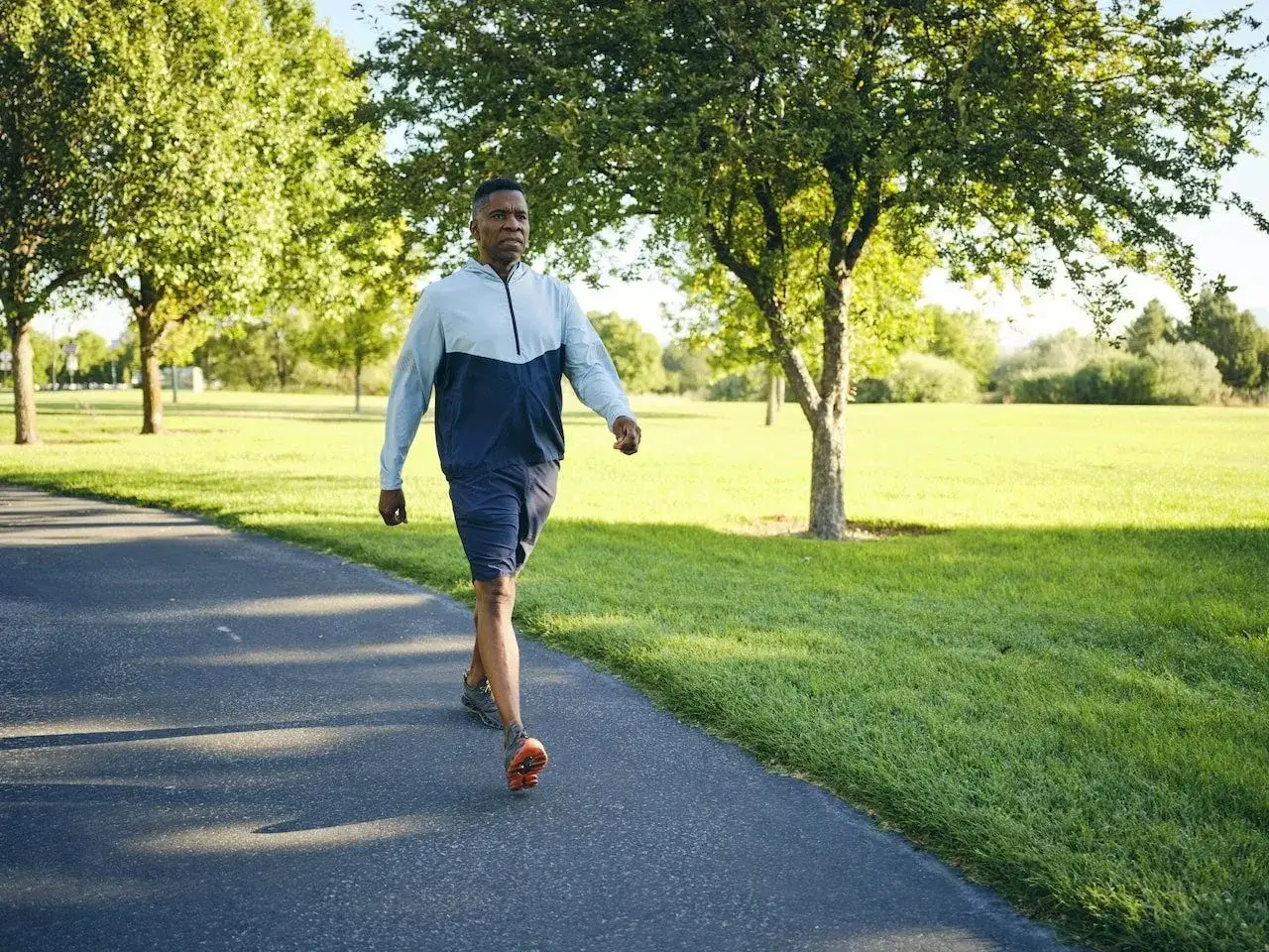 Mann joggt im Park, um abzunehmen. Sonnenschein und grüne Wiesen begleiten ihn auf seinem Weg.