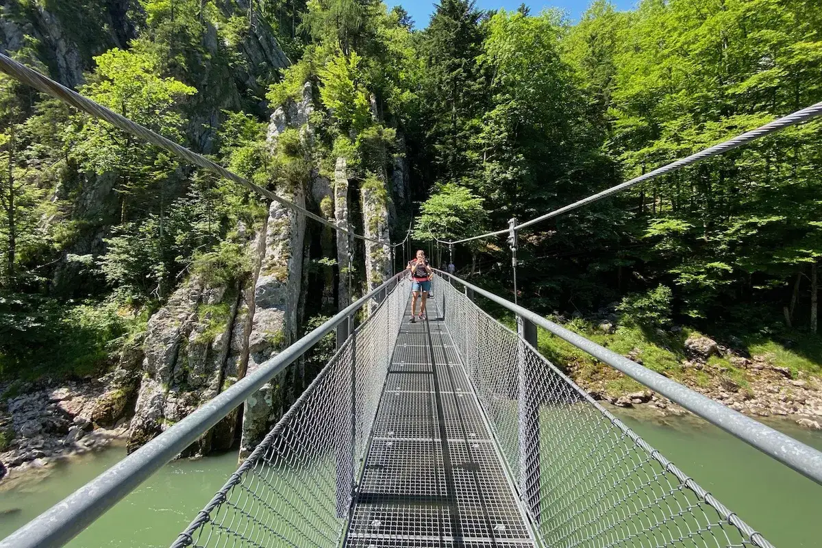 Frauen &uuml;berqueren eine H&auml;ngebr&uuml;cke w&auml;hrend einer entenlochklamm wanderung. Gr&uuml;ne B&auml;ume und Felsen s&auml;umen den Weg.
