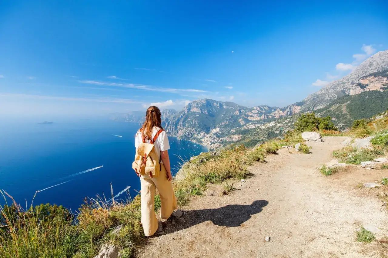 Frau mit Rucksack genießt den Ausblick auf die Küste Italiens. Ein perfekter Ort für fernwanderwege Italien.