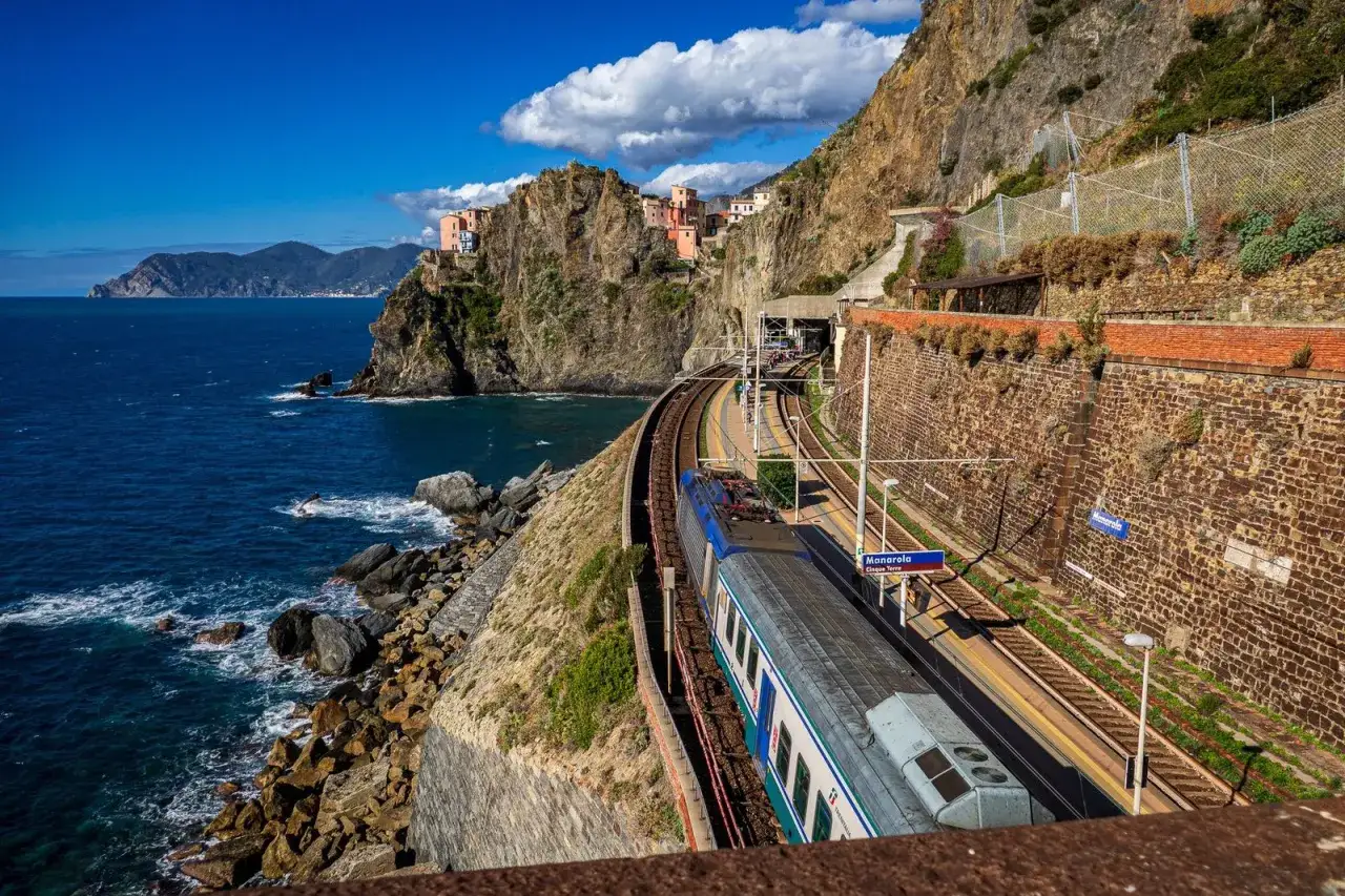 Zug hält in Manarola, einem der Cinque Terre Geheimtipps. Bunte Häuser kleben an steilen Felsen über dem blauen Meer.