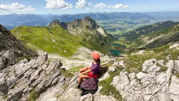 Ein Mädchen mit Rucksack genießt die Aussicht auf die Berge bei Oberstdorf. Ein leichtes Wandern mit toller Belohnung.