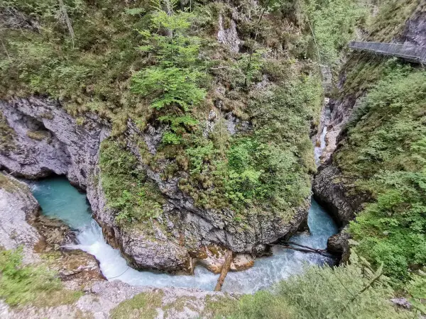 Türkisblaues Wasser rauscht durch eine enge Schlucht mit steilen Felswänden, bewachsen mit üppigem Grün. Eine Holzbrücke führt über die Klammen in Bayern.